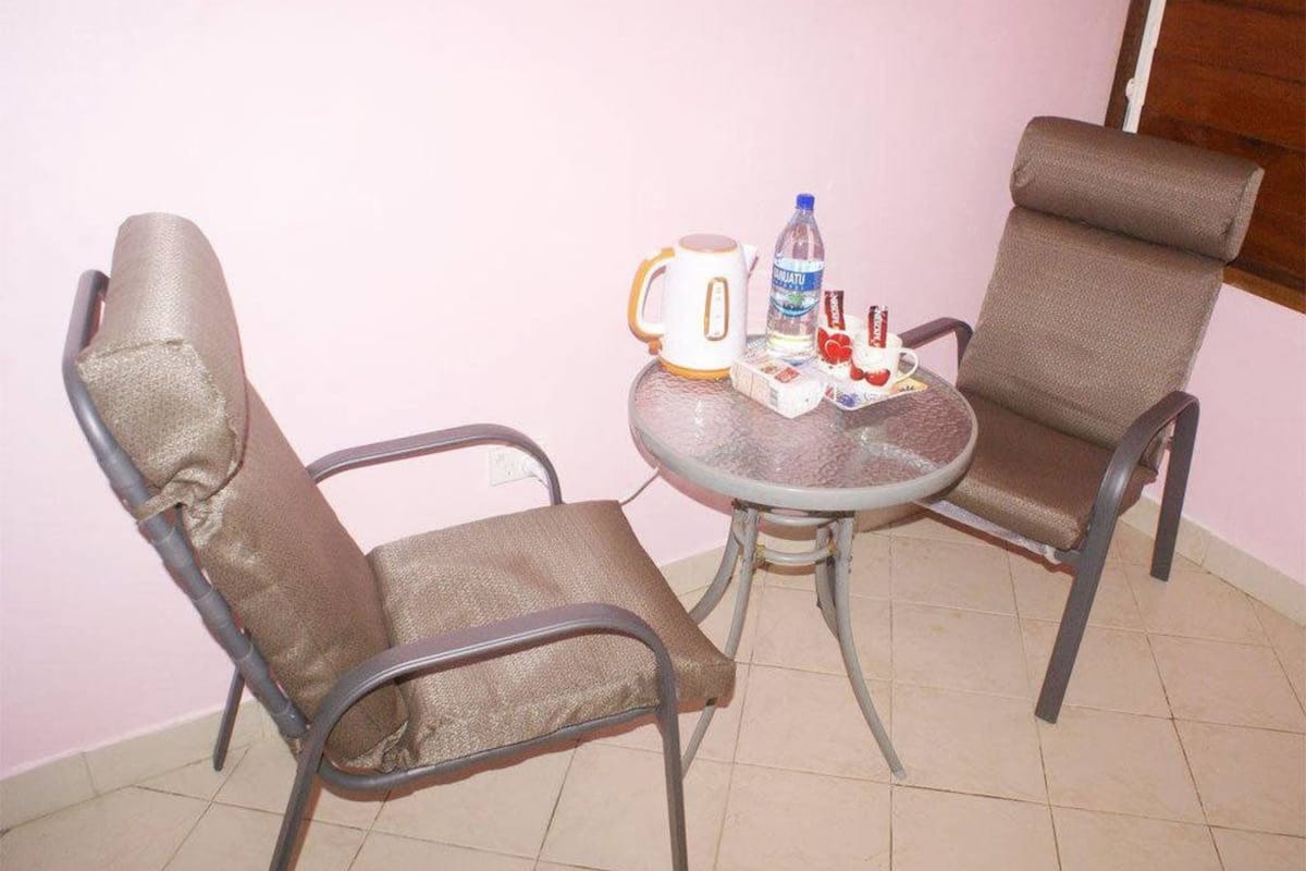 Two metal-framed chairs with cushioned seats and backs, a small round table with a coffee pot, a bottle of water, and some snacks.