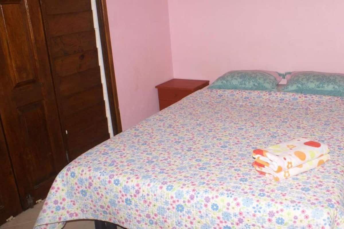 A bedroom with a floral bedspread, a wooden wardrobe, and a small bedside table.
