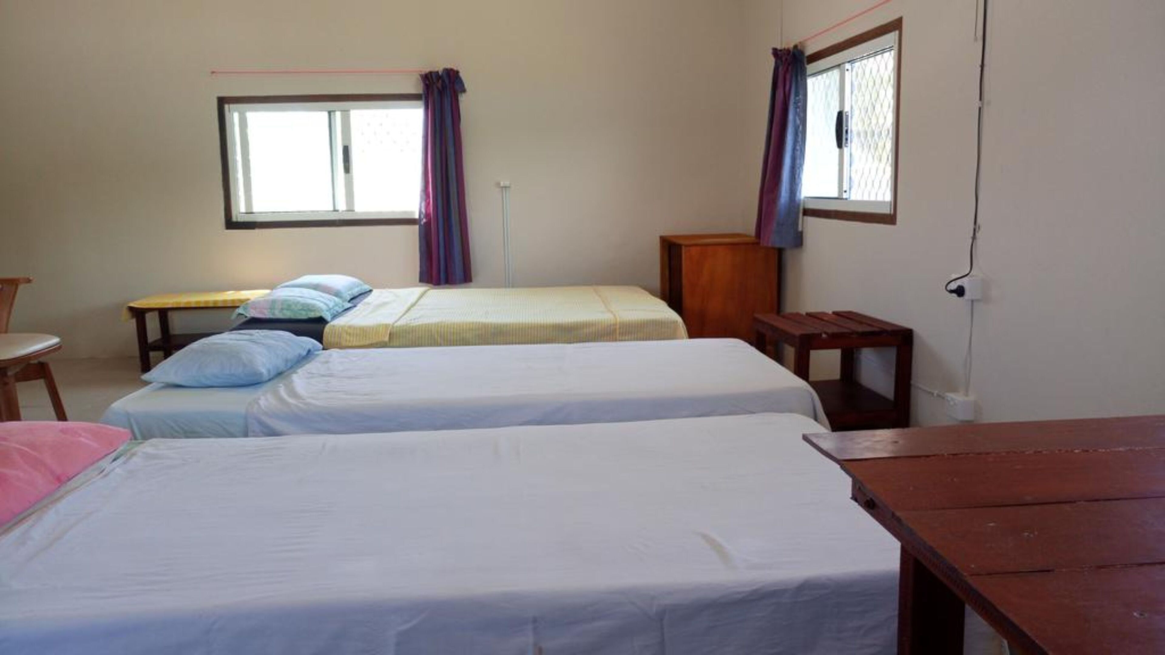 A room with two single beds, a small table, a chair, and a window with curtains.