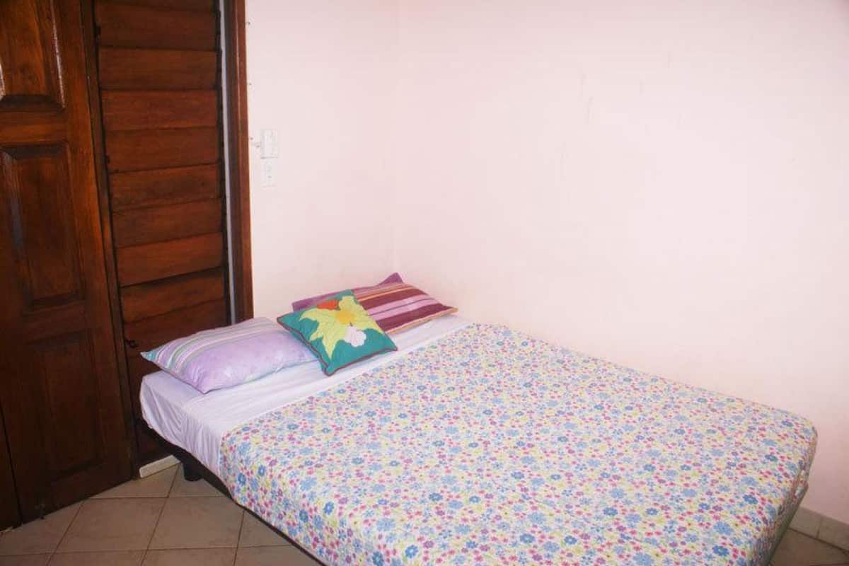 A small, single-bed room with a wooden door, a floral bedspread, and two pillows.
