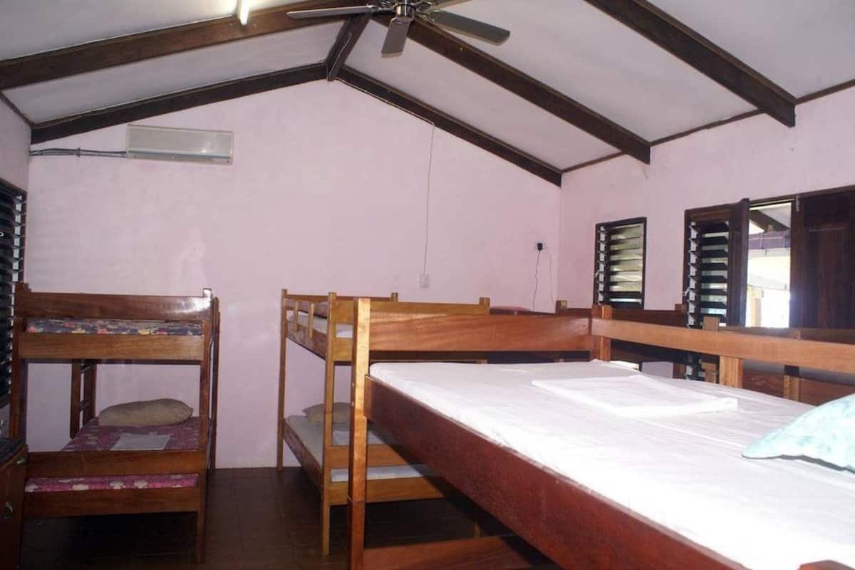 A dormitory room with bunk beds, a ceiling fan, and a window with shutters.