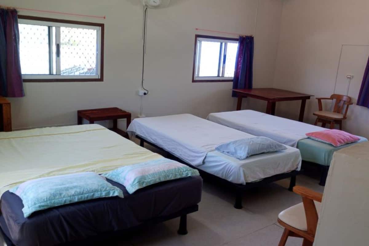 A dormitory room with three single beds, two small tables, and a chair.