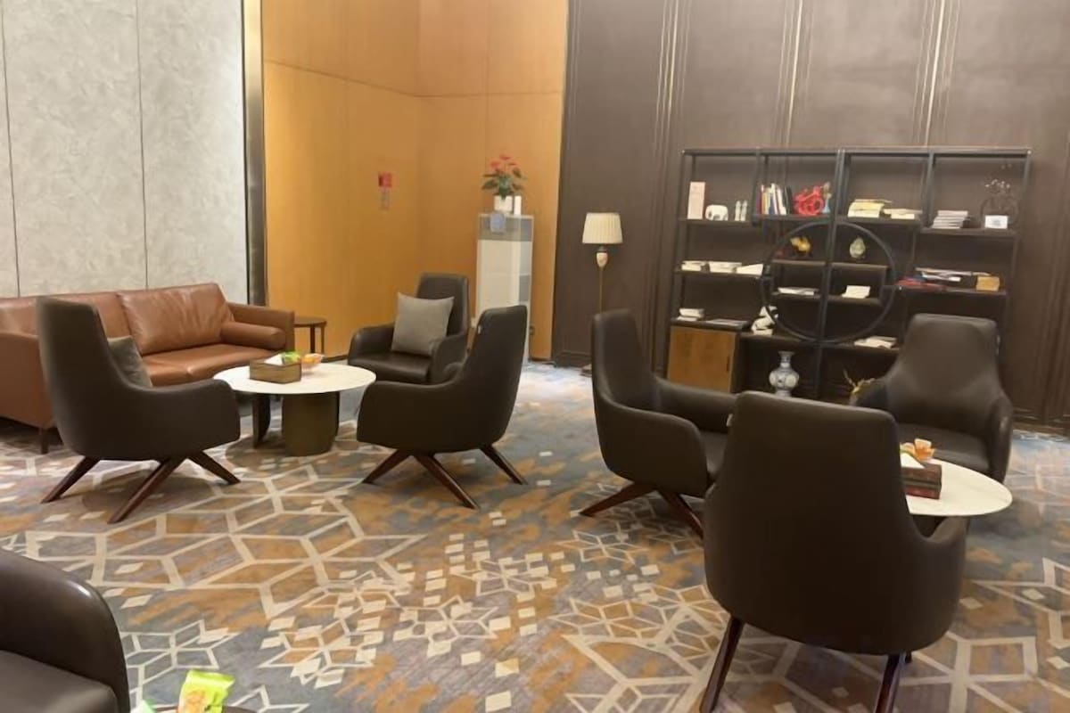 A lobby with a brown leather sofa, black armchairs, a coffee table, and a bookshelf.