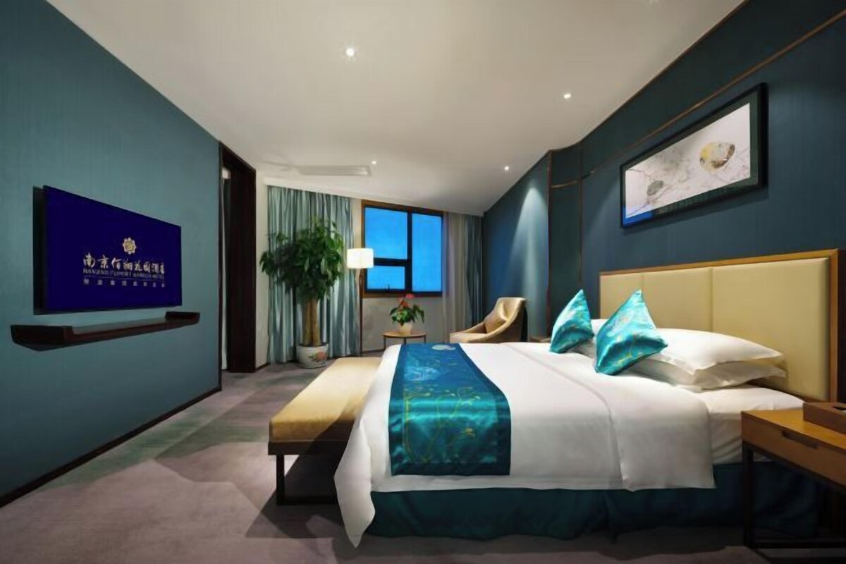 Una habitación de hotel con cama, mesita de noche, silla, televisor y planta.
