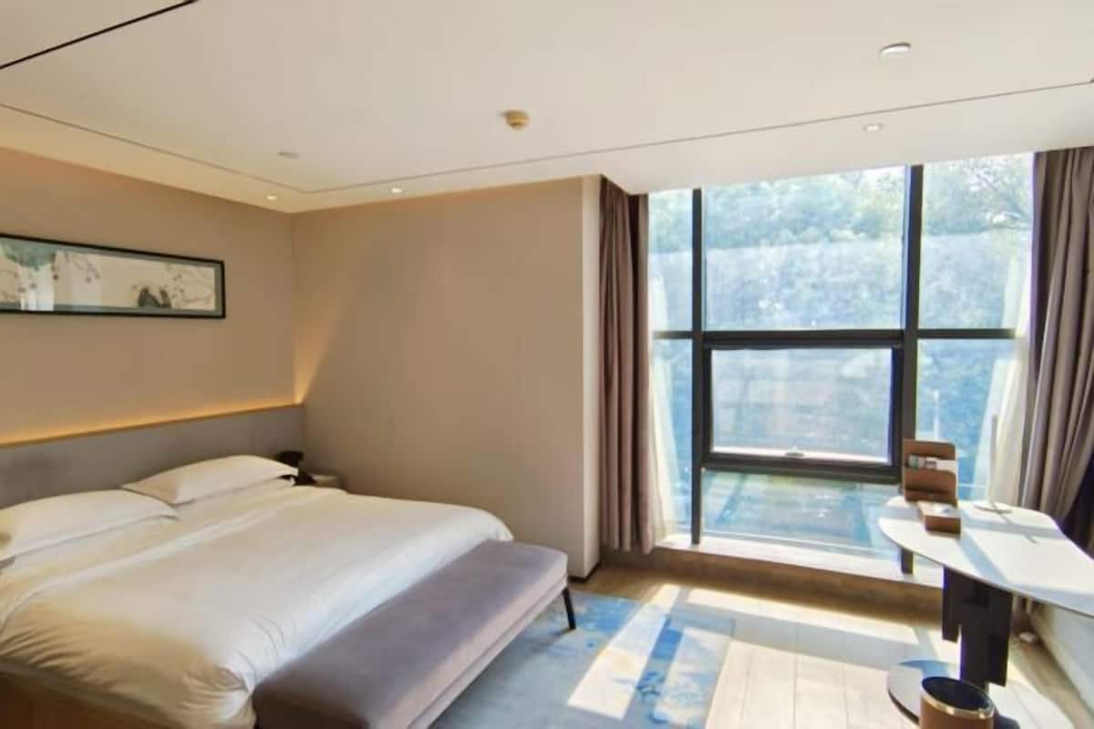 Une chambre d’hôtel moderne avec une grande fenêtre, un lit, une table de chevet et un petit bureau.