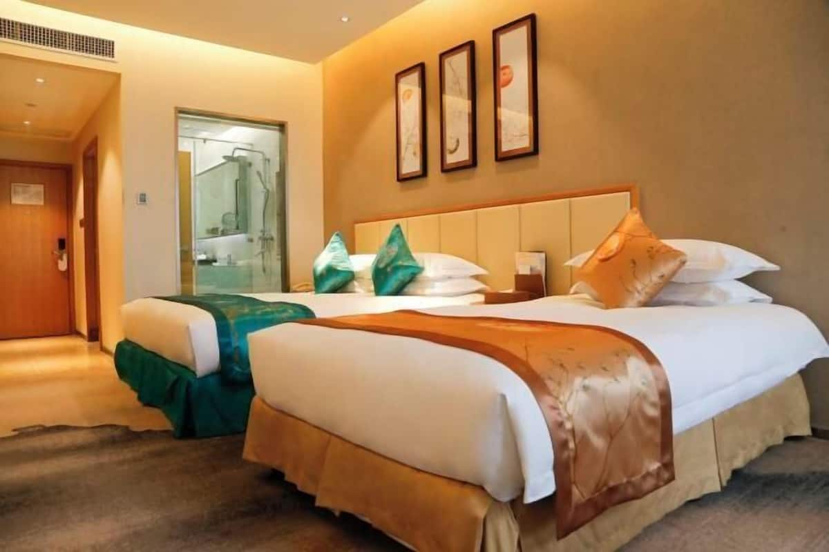 Une chambre d’hôtel avec deux lits, un espace douche et des œuvres d’art encadrées accrochées au mur.