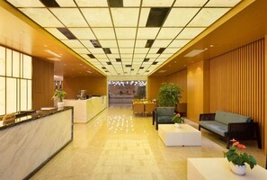 Een hotellobby met een receptiebalie, een zithoek en uitzicht op de eetruimte.