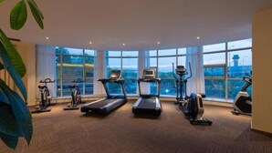 A gym with treadmills, stationary bikes, and an elliptical machine, large windows, and a plant. - Fliport Garden Hotel (Nanjing Lukou Airport Branch) (Nanjing)
