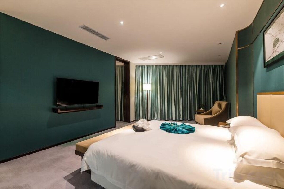 A hotel room with a large bed, a flat-screen TV mounted on the wall, a chair, and a window with curtains.