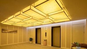 A hotel lobby with a geometric ceiling design, a reception desk, and two elevators.