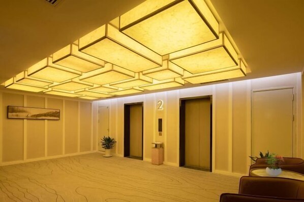 Un hall de hotel con un diseño geométrico en el techo, un mostrador de recepción y dos ascensores.