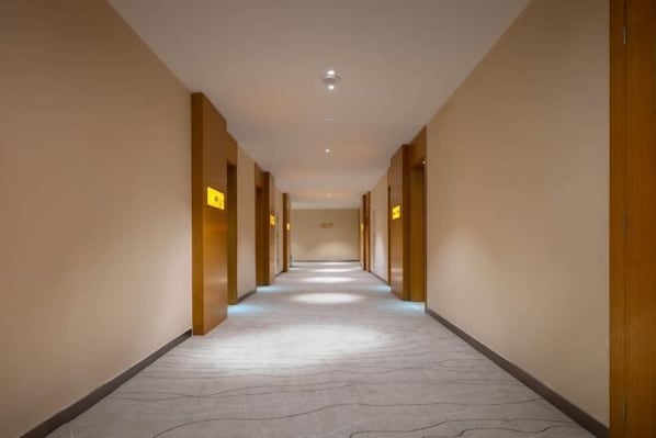 Un pasillo largo y estrecho con alfombra estampada y puertas de madera a ambos lados.