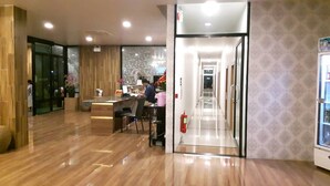Een hotel lobby met een receptiebalie, een brandblusser en een gang naar andere kamers.