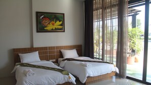 Hotelkamer met twee bedden, een houten hoofdbord, een lijst met een afbeelding van een vlinder en bloemen, en uitzicht op het landschap door grote ramen.