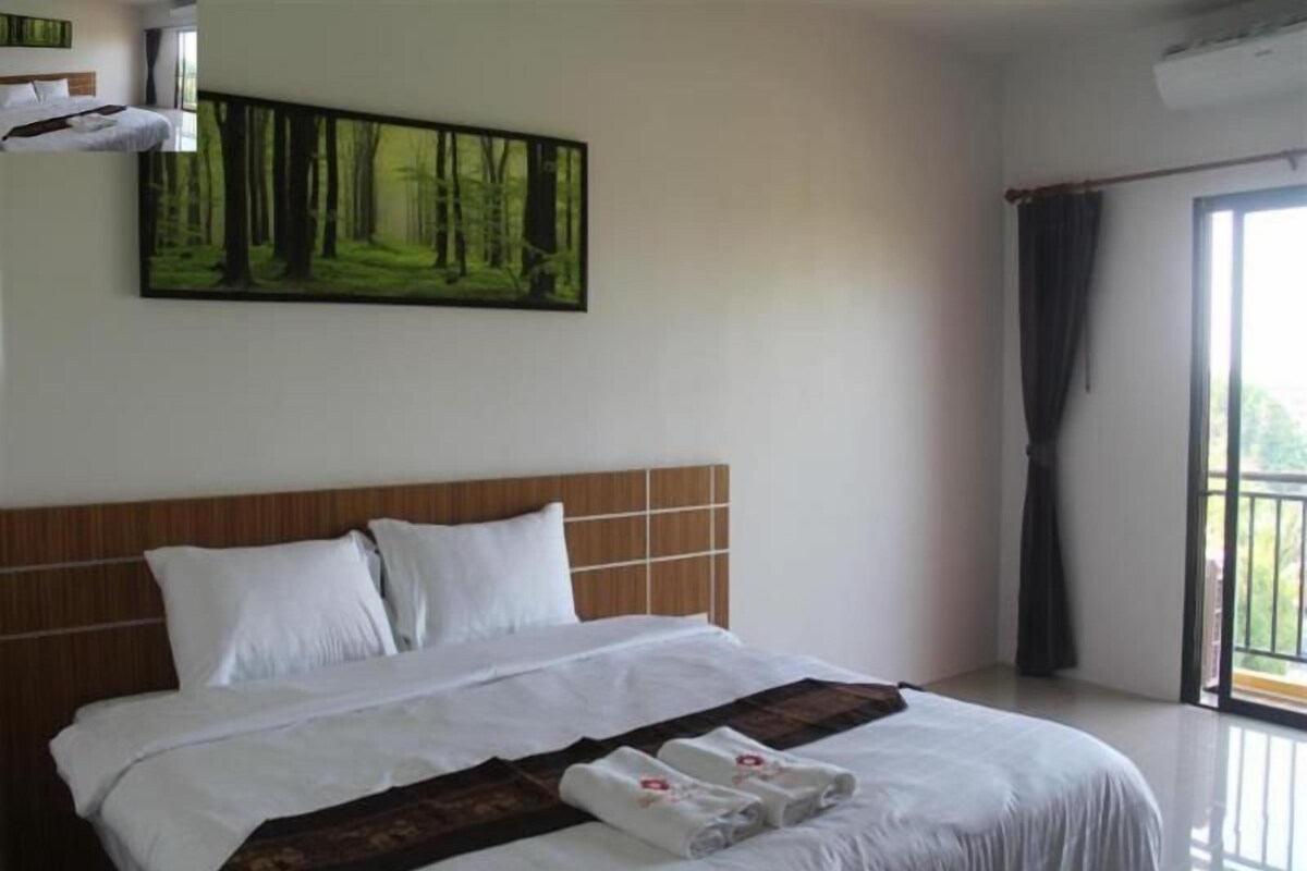Habitación de hotel con una cama grande, un cuadro de un bosque, una ventana con cortinas y un balcón.