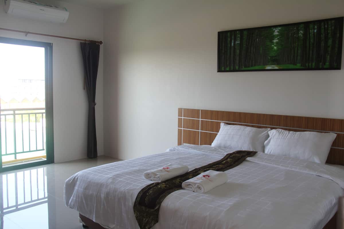A hotel room with a bed, a painting on the wall, and a window with curtains.