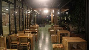 Een restaurant met houten tafels en stoelen in rijen, een groene vloer en potplanten.