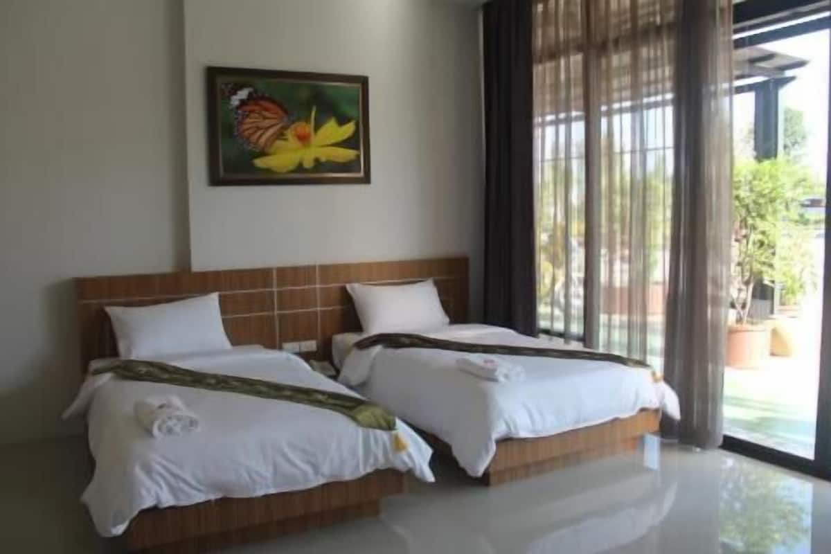 A hotel room with two beds, a painting of a butterfly and flower on the wall, and a view of greenery through the window.