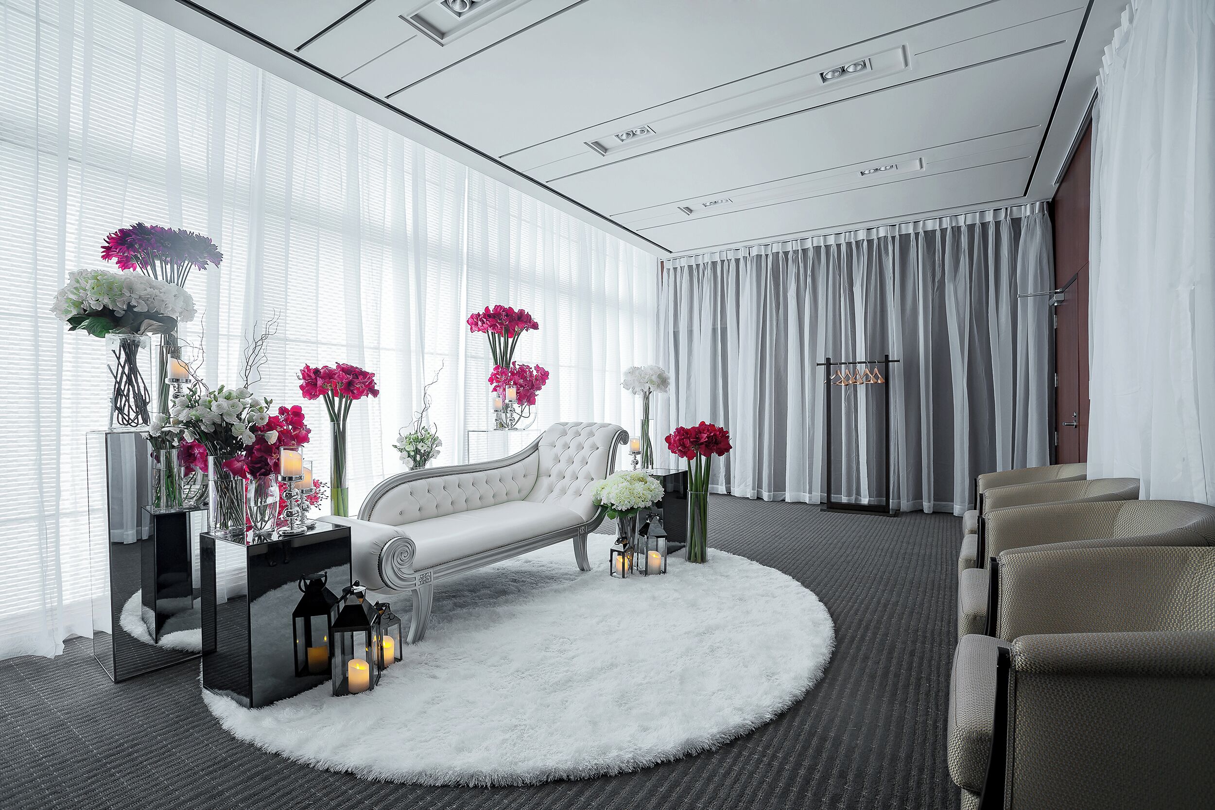 Una habitación de hotel moderna con un sofá blanco, un tapete redondo y un ventanal con cortinas de gasa.