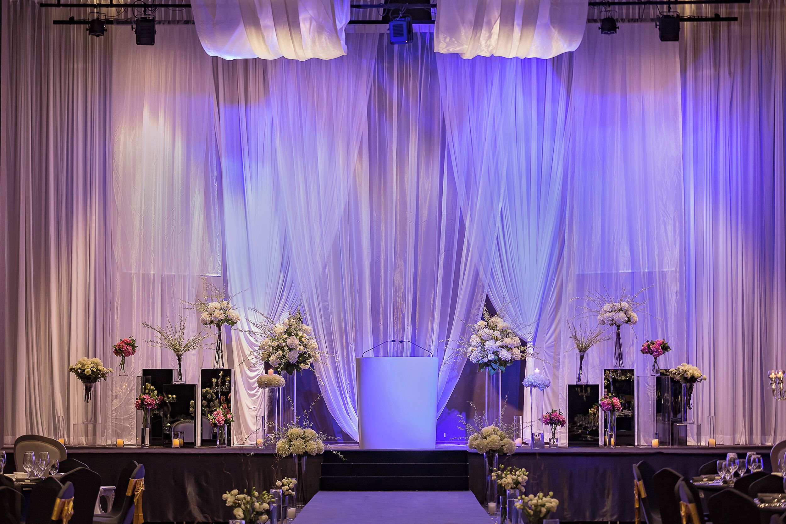 A stage with a podium, draped curtains, and floral arrangements.