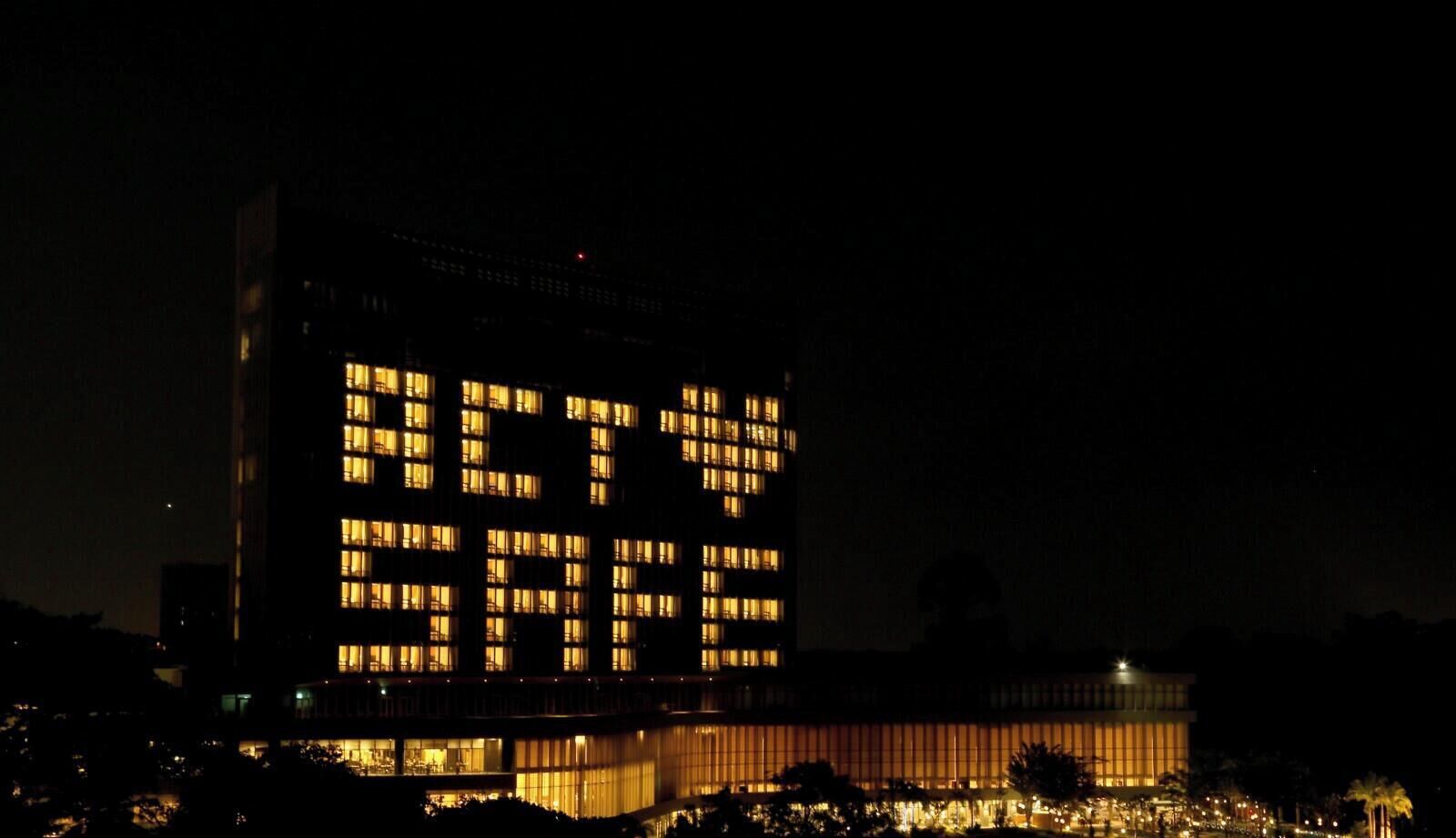 Un bâtiment dont les fenêtres illuminées forment le texte « AGISSEZ MAINTENANT ».