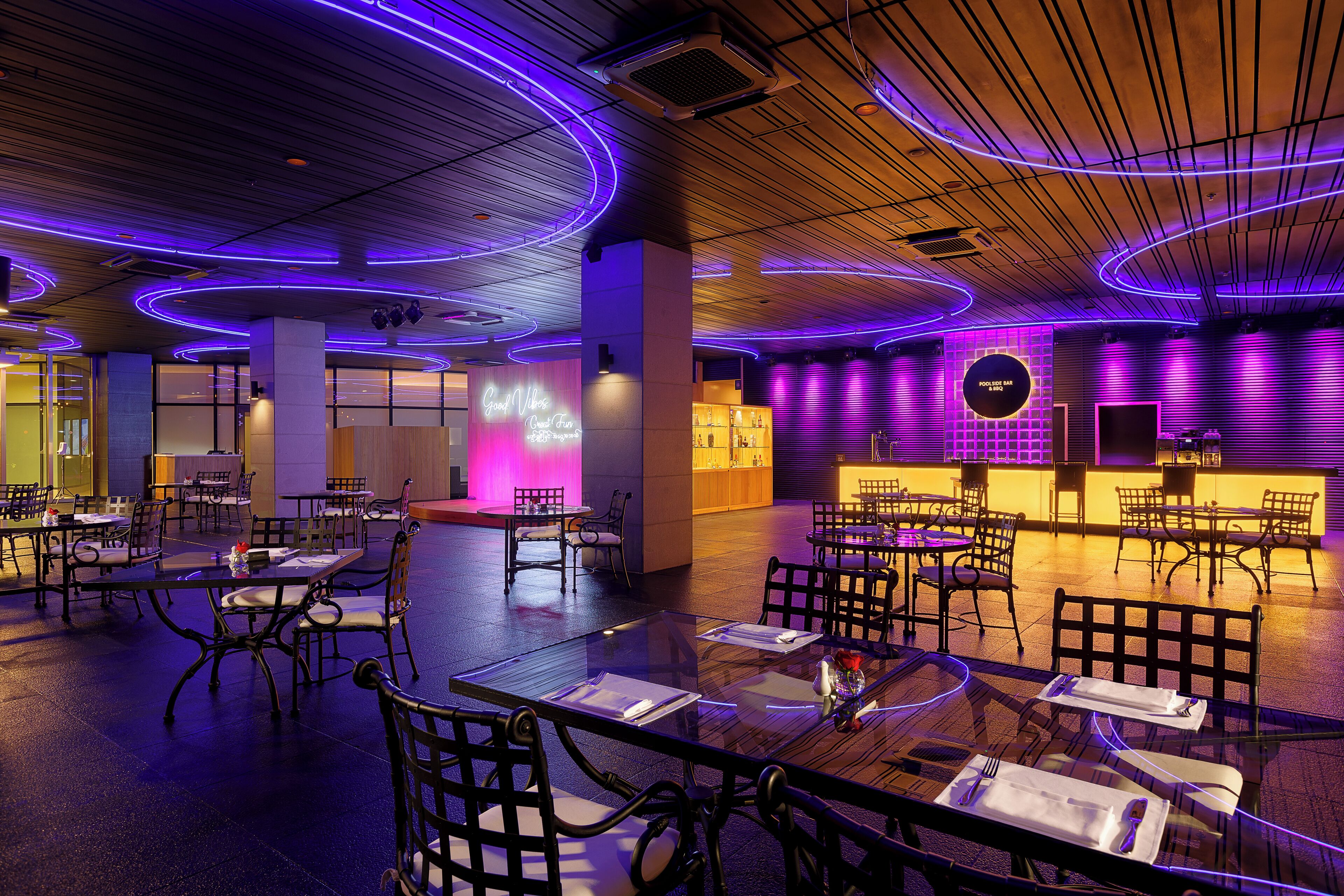 Un amplio comedor interior con mesas y sillas, una recepción y un techo iluminado con neón.