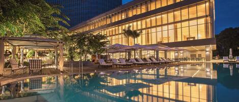 Un hotel con piscina, tumbonas y una zona cubierta con sombrillas.