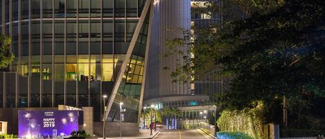 A modern hotel with a curved glass facade, a well-lit entrance, and a festive New Year display.