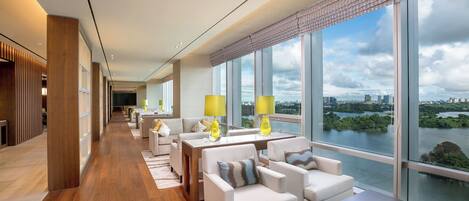 A modern hotel lobby with a long corridor, seating area, and large windows offering a view of a river and cityscape.
