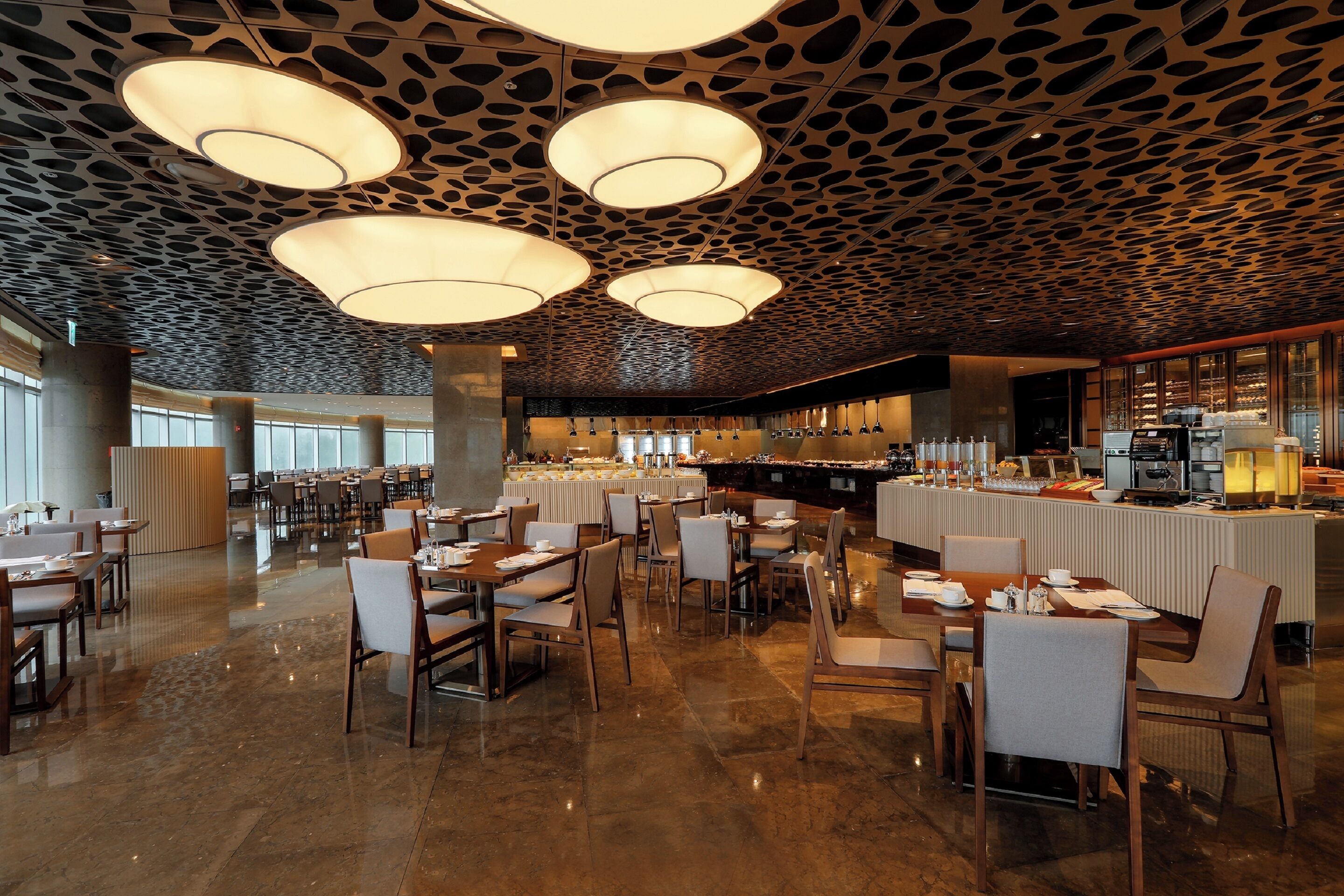 Een ruime eetruimte met meerdere tafels en stoelen, een centraal buffet en een opvallend plafondontwerp.