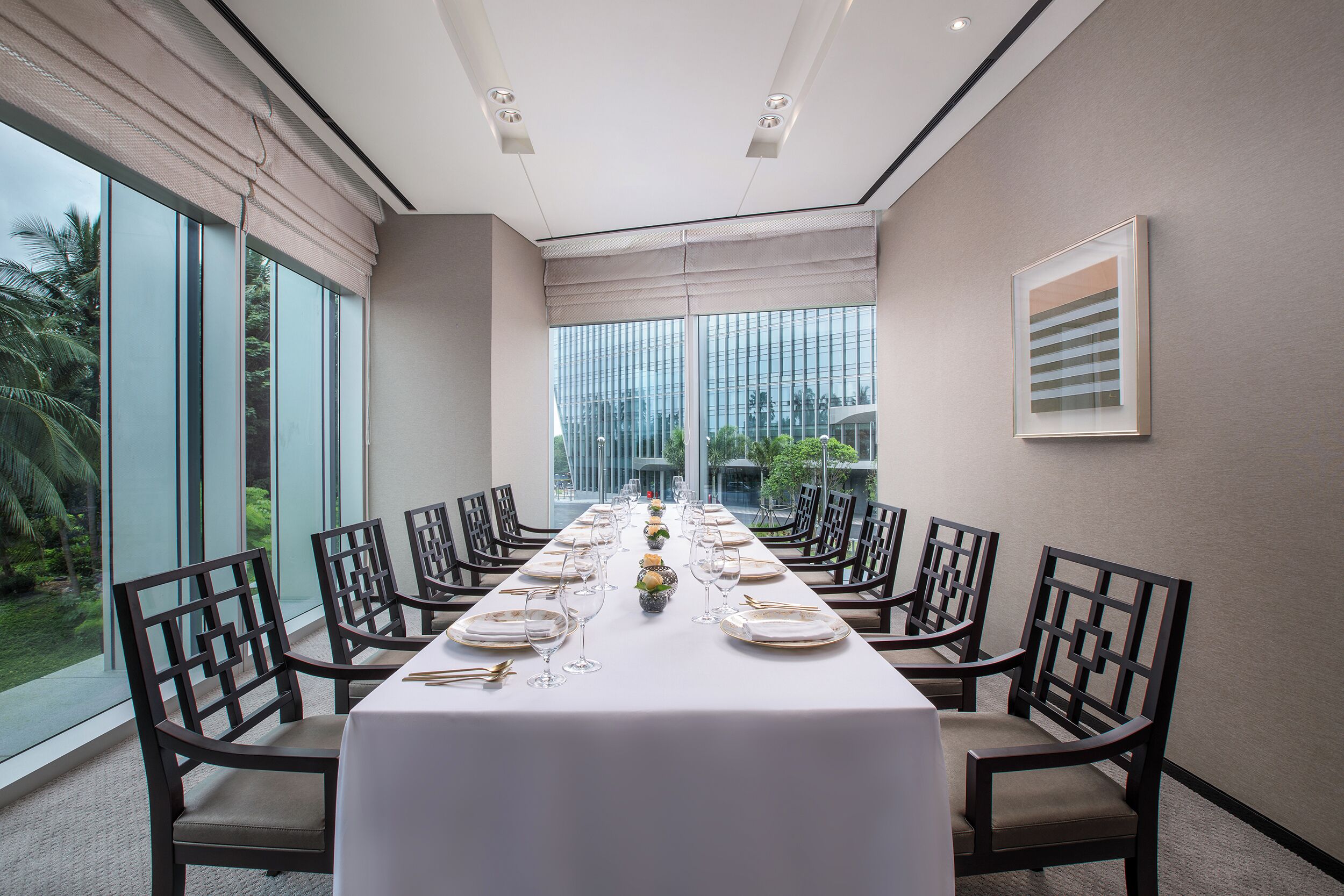 A long dining table set with chairs, large windows, and a view of greenery outside.