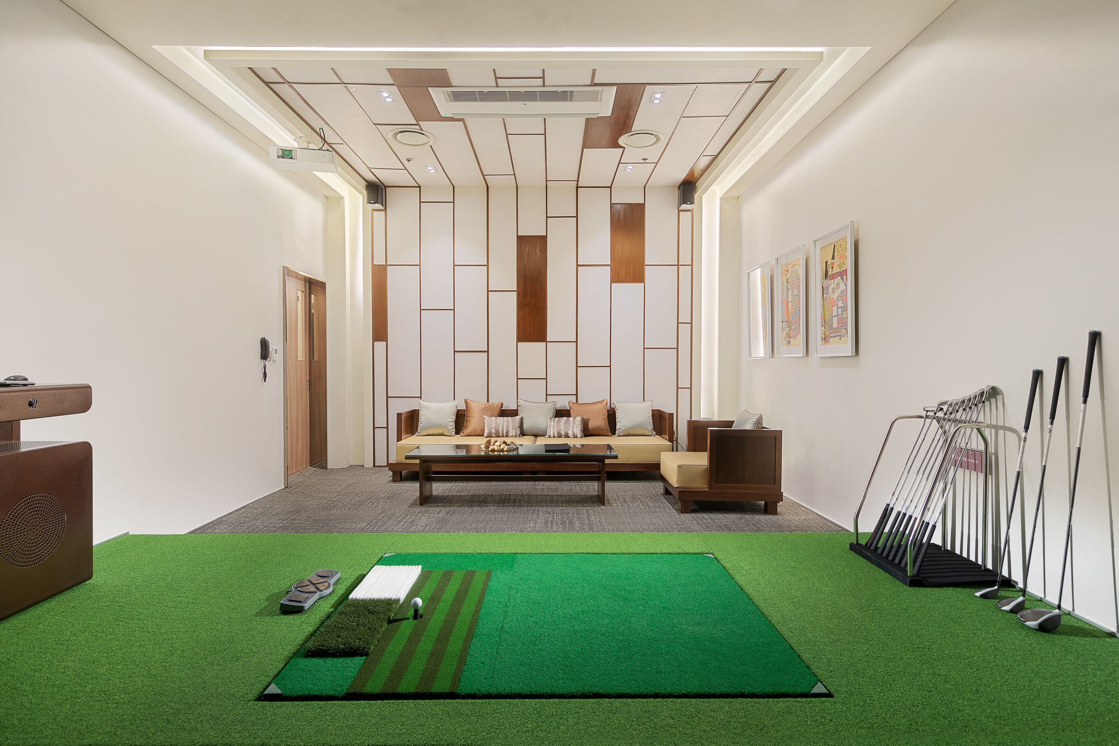 A modern hotel lobby with a green artificial turf area, a sofa set, a coffee table, and a golf club rack.