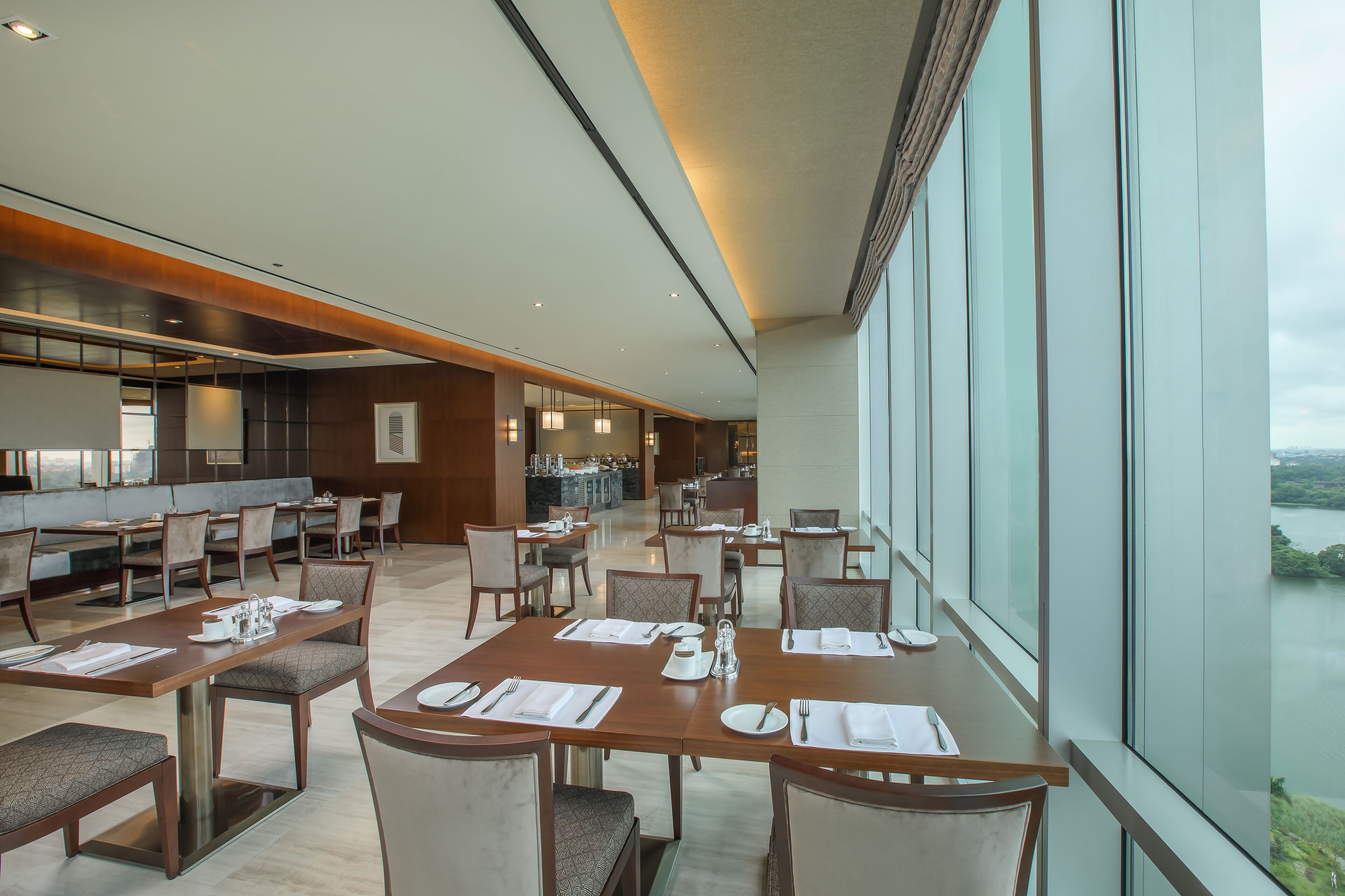 A modern dining area with multiple tables set for service, large windows offering a view of the outdoors, and a contemporary interior design.
