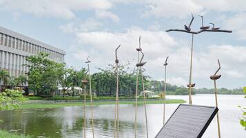 A serene lakeside view with a modern building in the background, a bamboo sculpture, and a signboard.