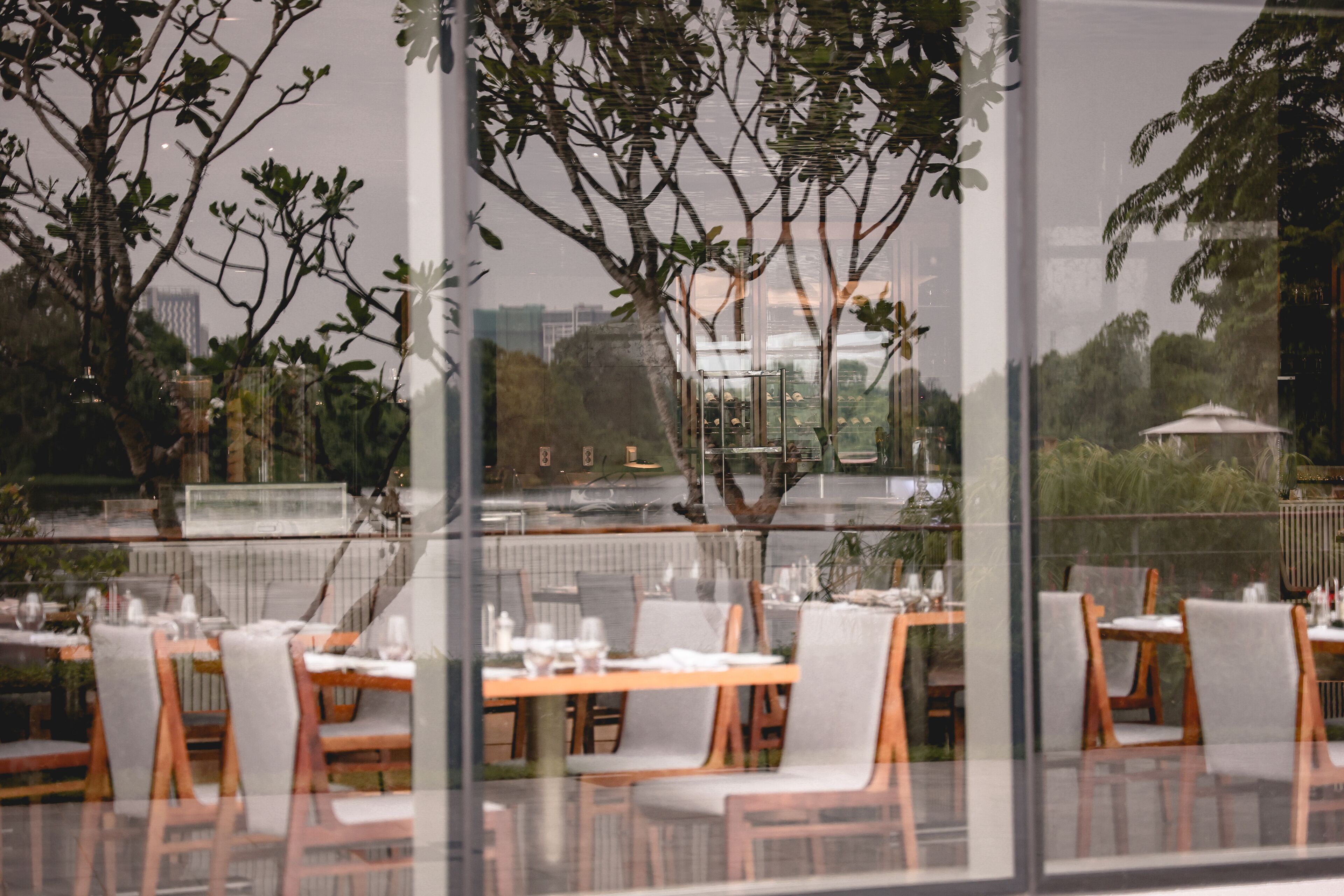 A restaurant with tables and chairs, large windows, and a view of trees and buildings.