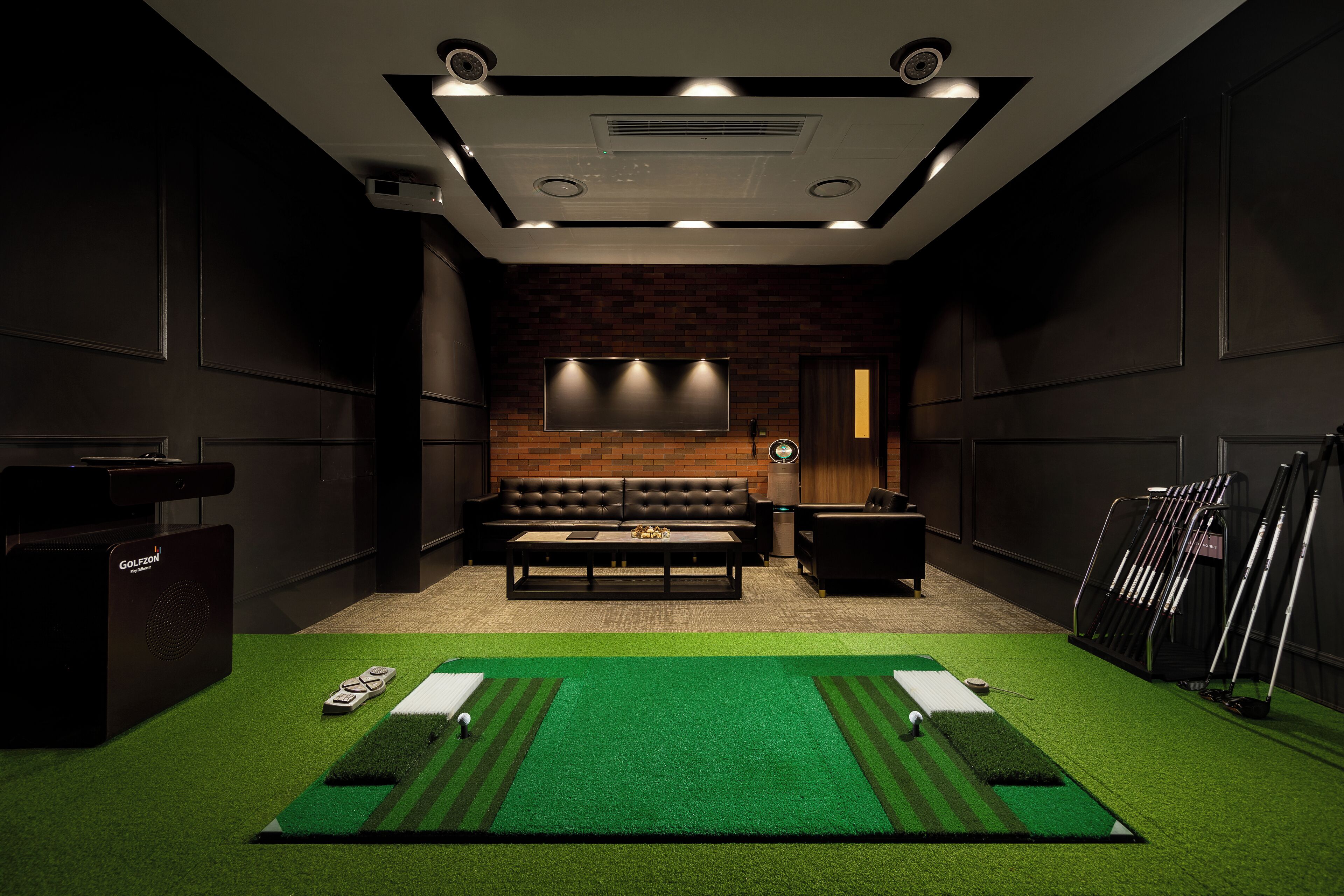 Una habitación con zona de césped artificial verde, sofá de cuero, televisor montado en la pared y un carrito de golf.