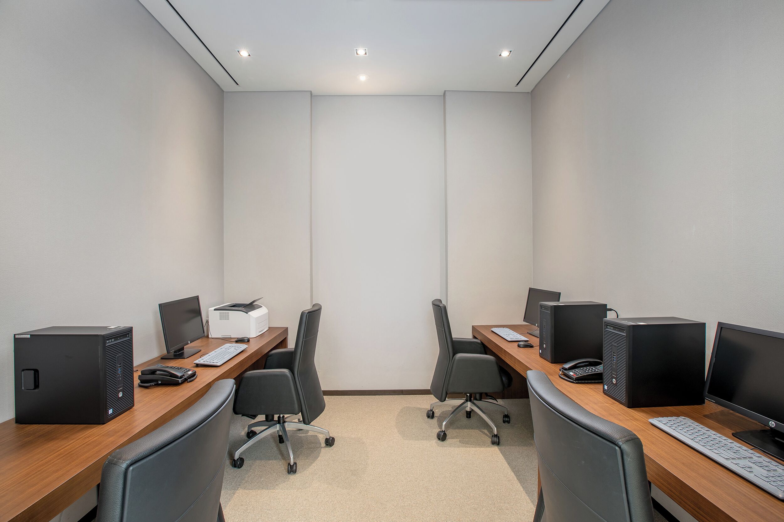 A conference room with four desks, each equipped with a computer, keyboard, and mouse.