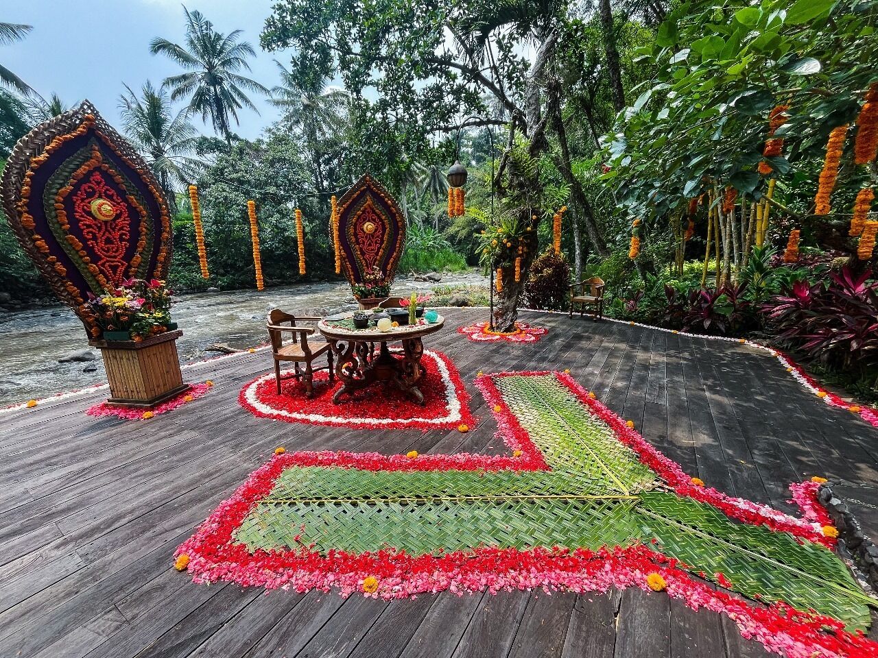 A wooden deck with a central table and chairs, surrounded by floral arrangements and a patterned carpet.