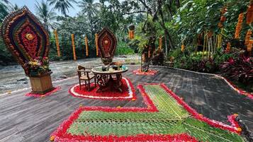 A wooden deck with a central table and chairs, surrounded by floral arrangements and a patterned carpet.