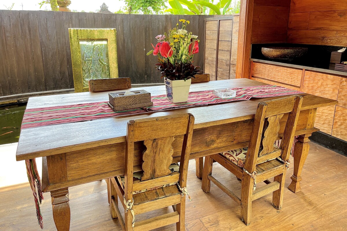 A wooden dining table with chairs, a vase with flowers, and a woven basket.