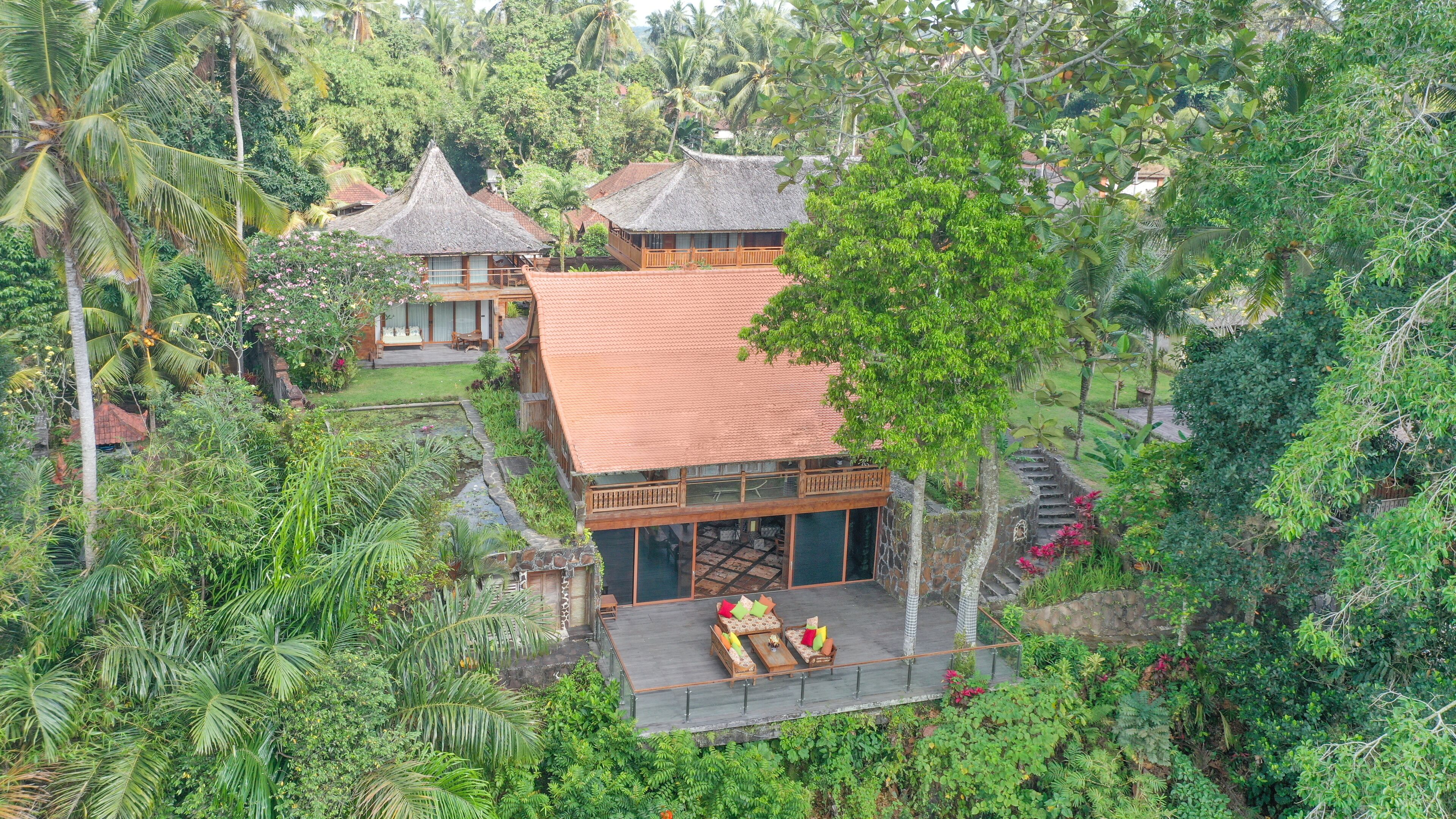 Um resort tropical com um edifício de telhado de palha, uma área de estar coberta ao ar livre e vegetação exuberante.
