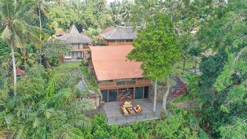 Um resort tropical com um edifício de telhado de palha, uma área de estar coberta ao ar livre e vegetação exuberante.