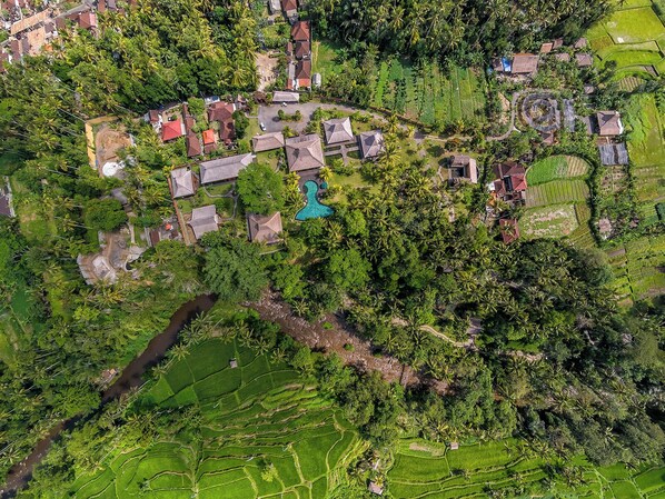 Vista aérea de un pueblo rural con campos en terrazas, una piscina central y casas dispersas.