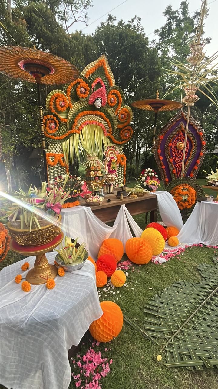 An outdoor event setup with a decorated table, floral arrangements, and a backdrop featuring a large, ornate structure.
