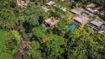 An aerial view of a resort with a swimming pool, thatched-roof buildings, and dense tropical vegetation.
