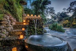 A stone water feature with cascading water, surrounded by moss-covered rocks and illuminated by lanterns. - Permata Ayung Private Estate (Ubud)