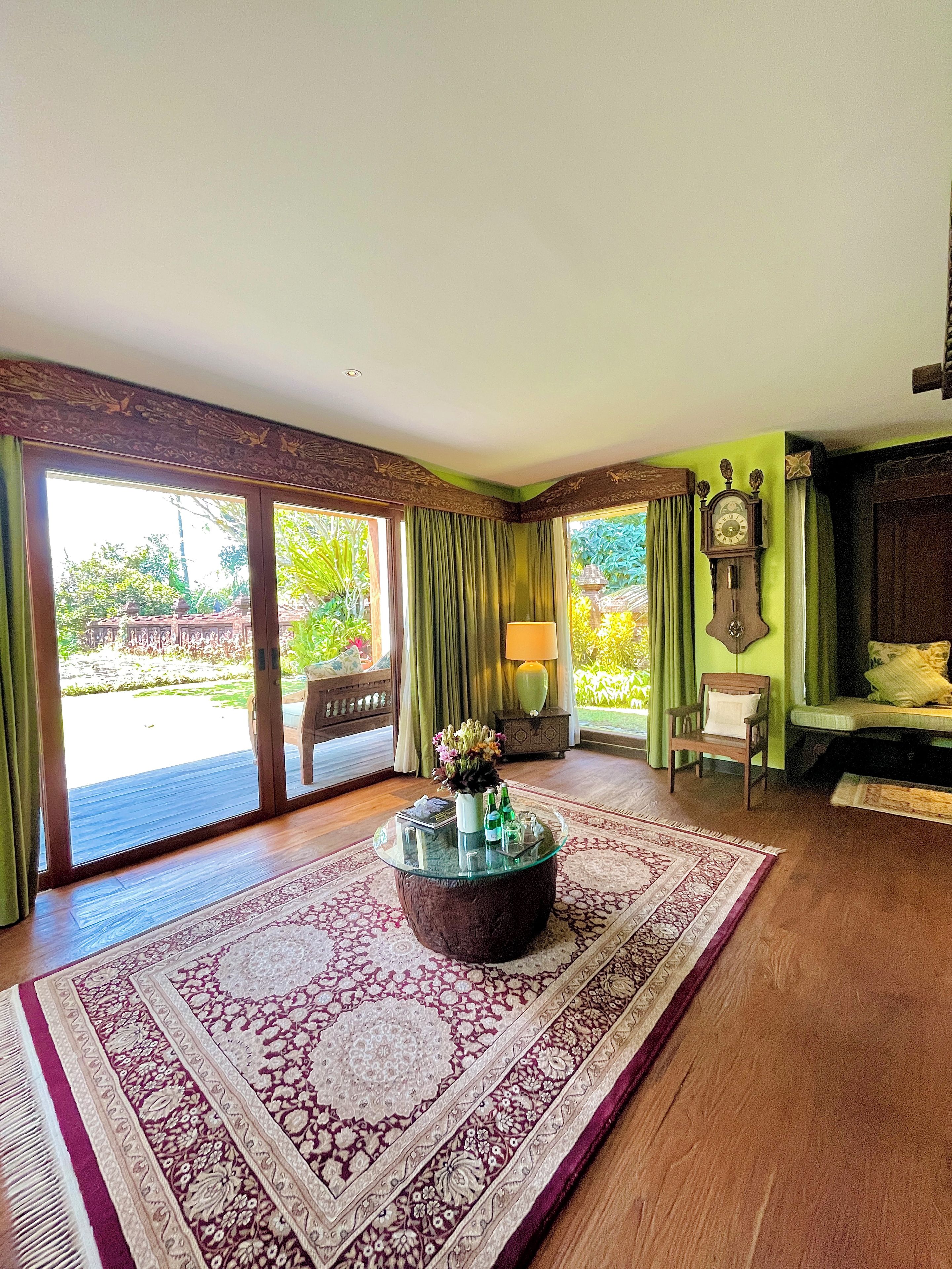 A room with a glass-top coffee table, a patterned rug, a wooden bench, and a view of a garden through large sliding doors.