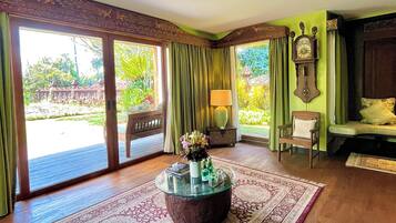 A room with a glass-top coffee table, a patterned rug, a wooden bench, and a view of a garden through large sliding doors.