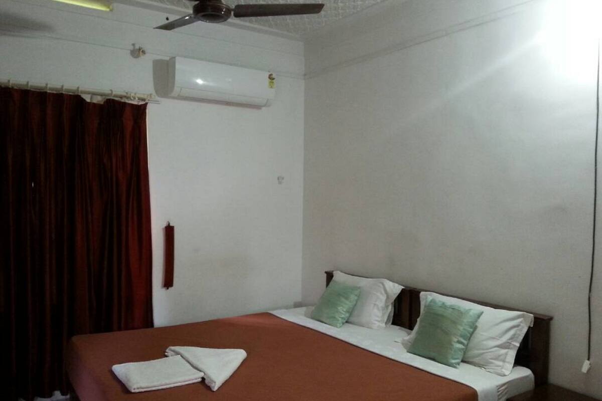 A bedroom with a bed, white curtains, a ceiling fan, and an air conditioning unit.