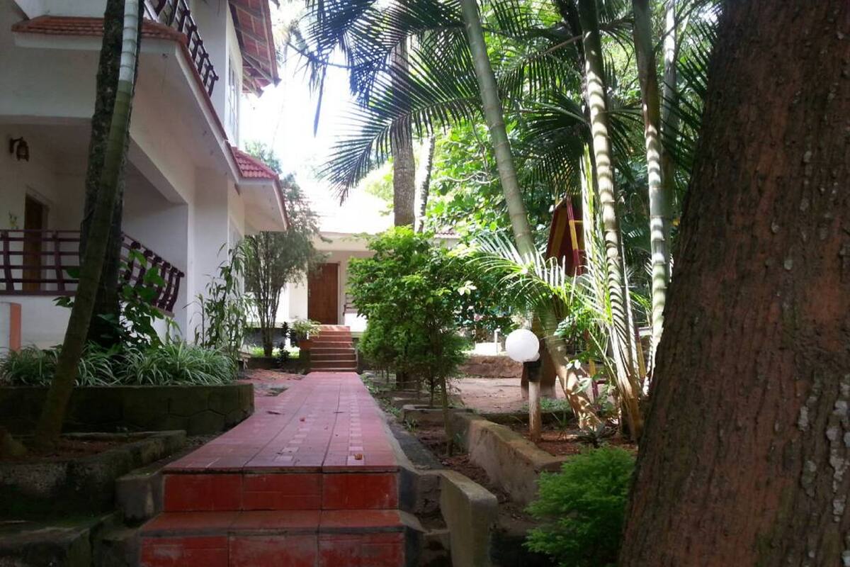 A pathway leading to a building with a red brick entrance, surrounded by tropical vegetation and palm trees.